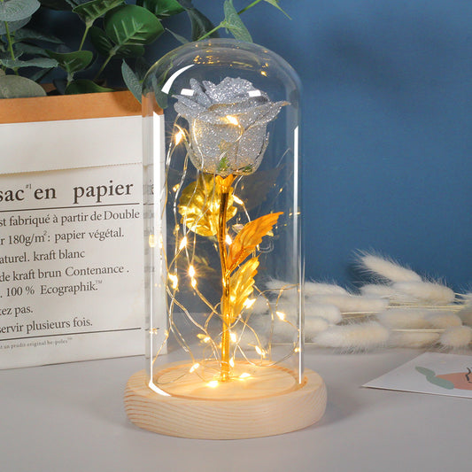 Gold rose in a glass dome with LED lights on a wooden base, against a blue wall with text and decor.
