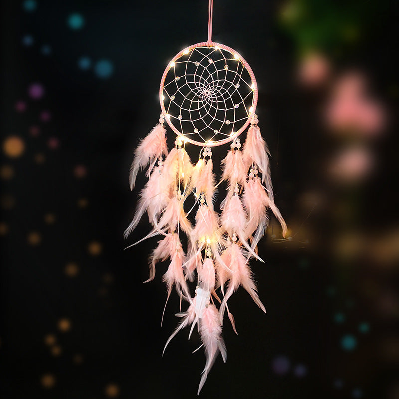 Pink dreamcatcher with feathers against a dark background