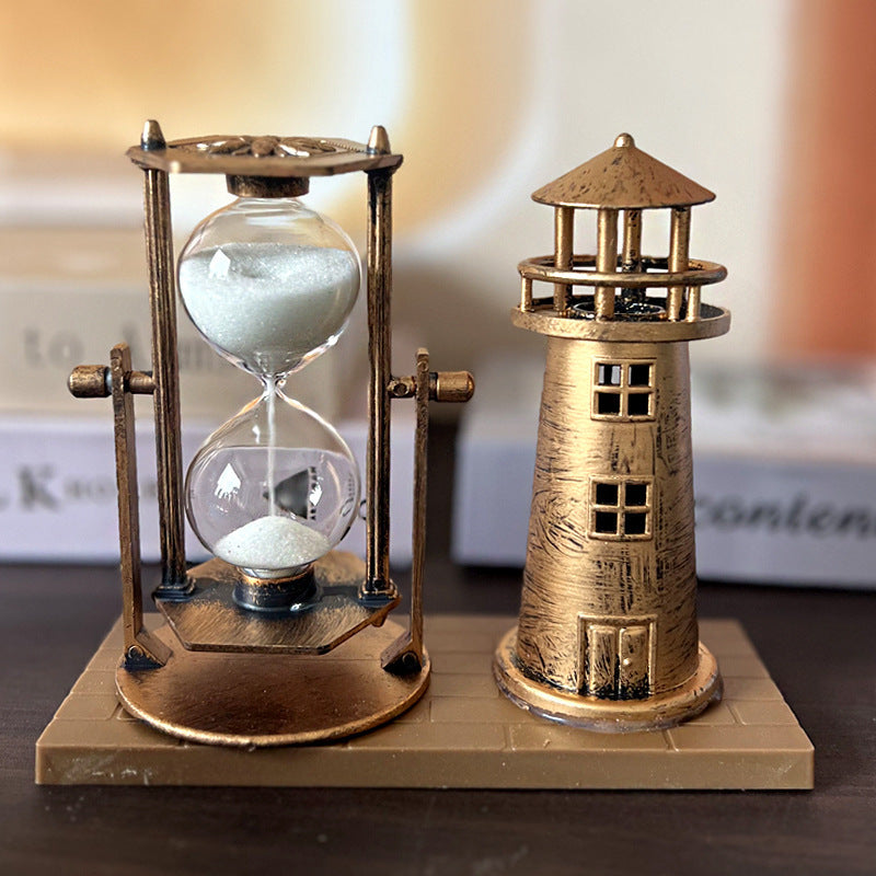 Decorative sand hourglass and lighthouse sculpture on a wooden base.
