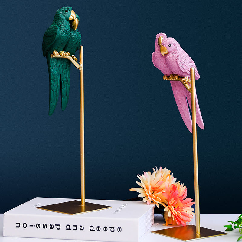 Two parrot figurines, one green and one pink, on gold stands with a dark blue background.