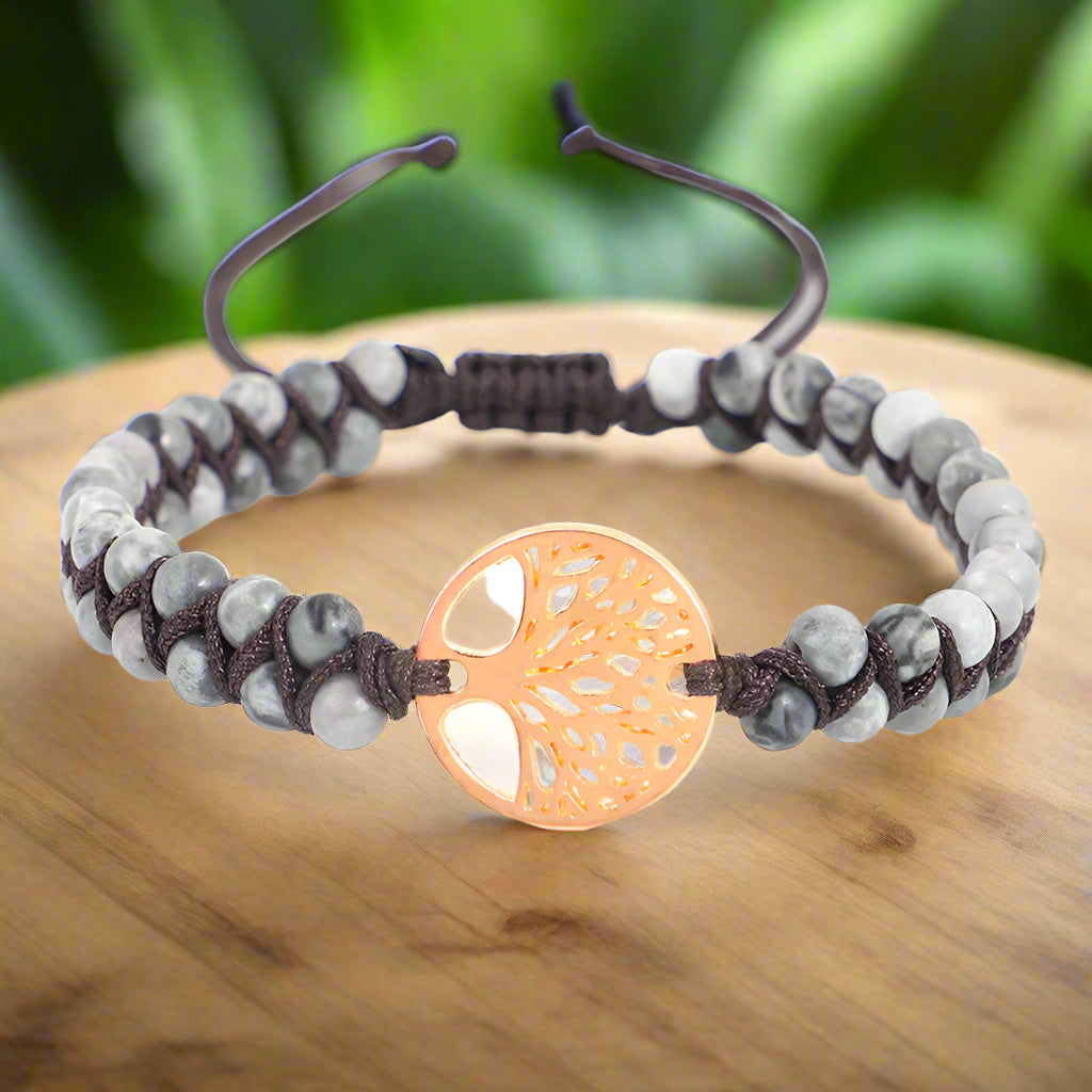Bracelet with gray beads and a rose gold tree-of-life charm on a white background