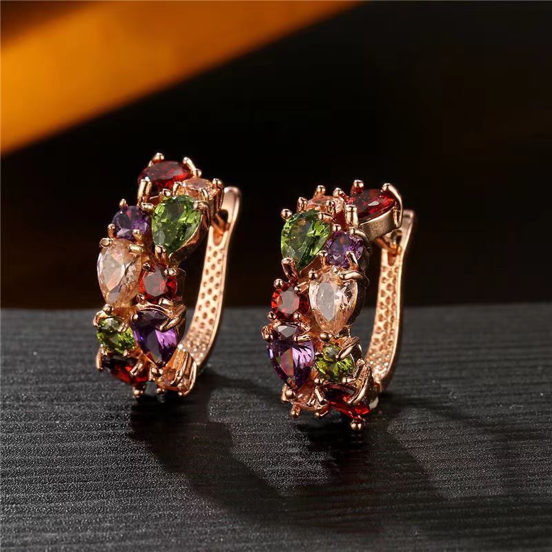 Pair of gold hoop earrings with multicolored gemstones on a dark surface.