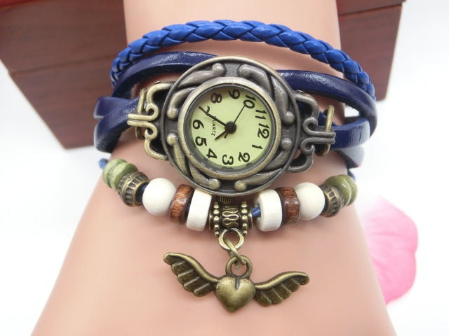 Multicolored bracelet with a vintage-style watch face and winged heart charm on a wrist.