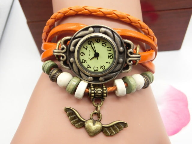 Multicolored braided bracelet with a vintage-style watch face and heart-shaped pendant on a wrist.