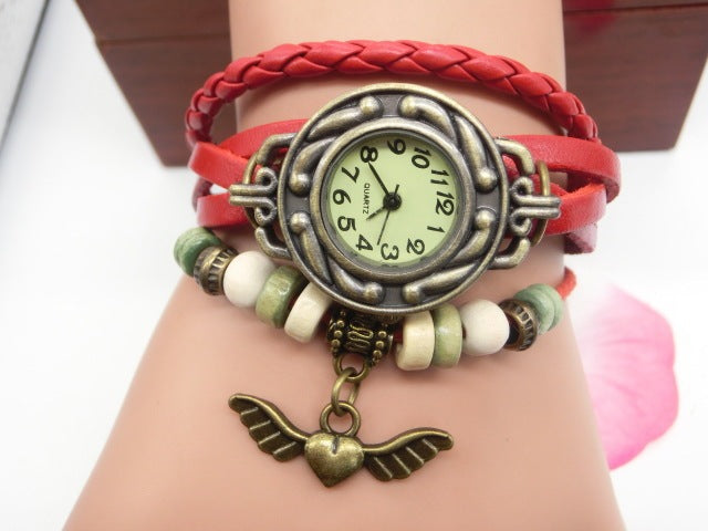 Bracelet with vintage-style watch face and wing charm on a wrist against a white background