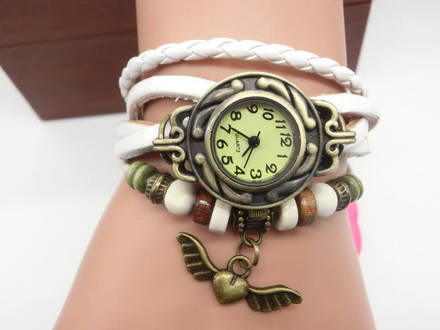 Wrist wearing a decorative watch with a white braided strap and wing charm on a plain background