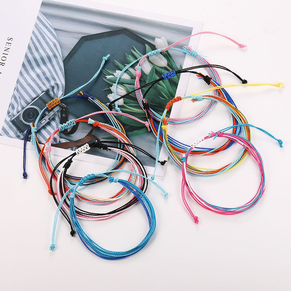 Colorful bracelets on a white surface with a striped bag and flowers in the background.