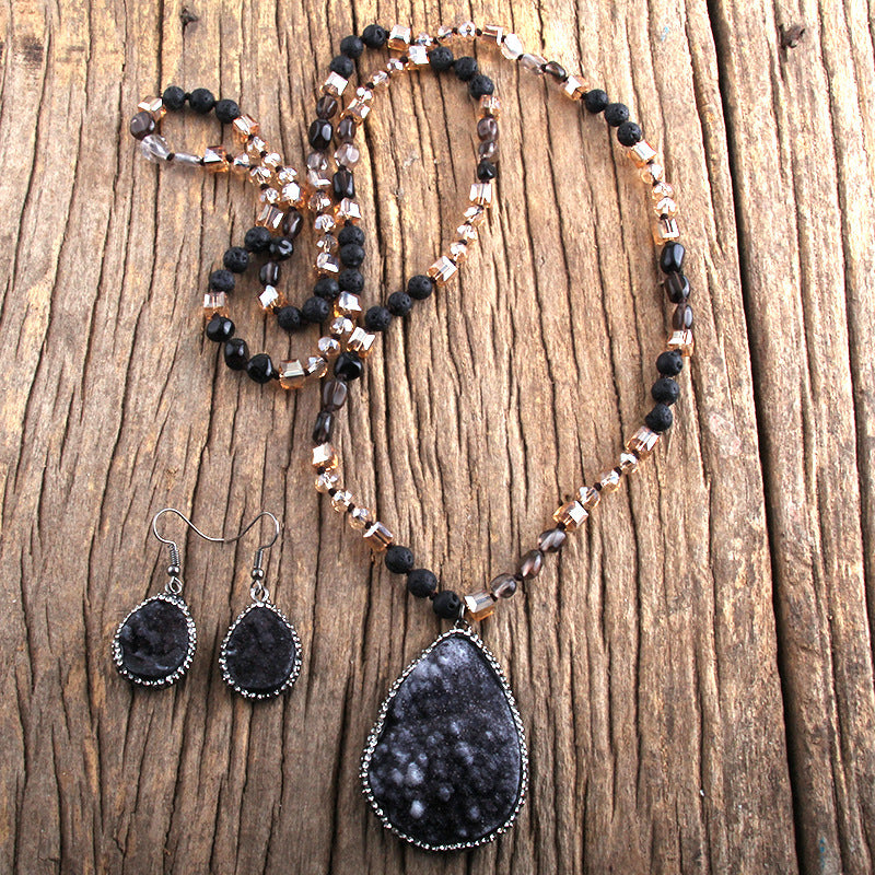 Necklace and earrings with black teardrop pendants on a wooden surface