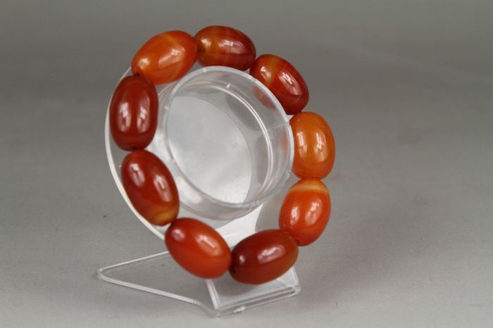 Bracelet with orange beads on a clear stand against a gray background