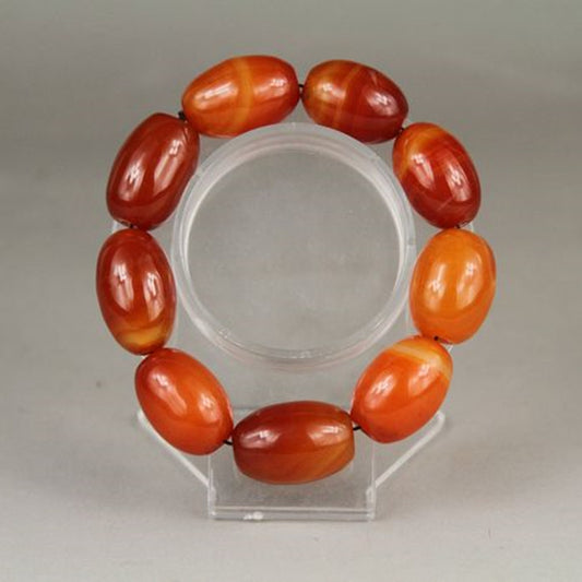 Bracelet with red and orange beads on a clear stand against a gray background