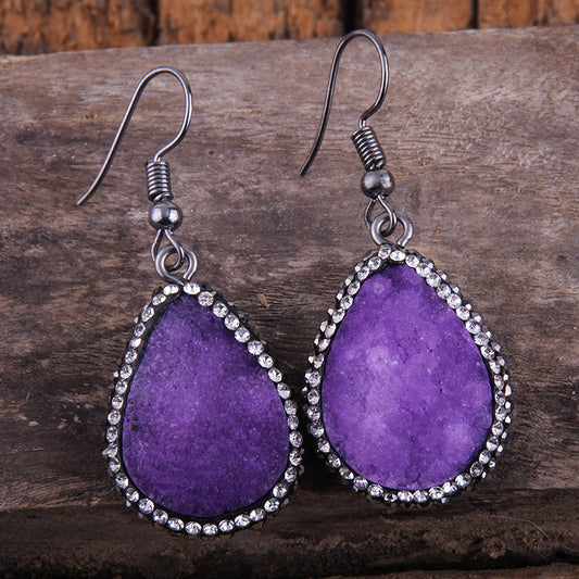 Purple teardrop earrings with silver accents on a wooden surface
