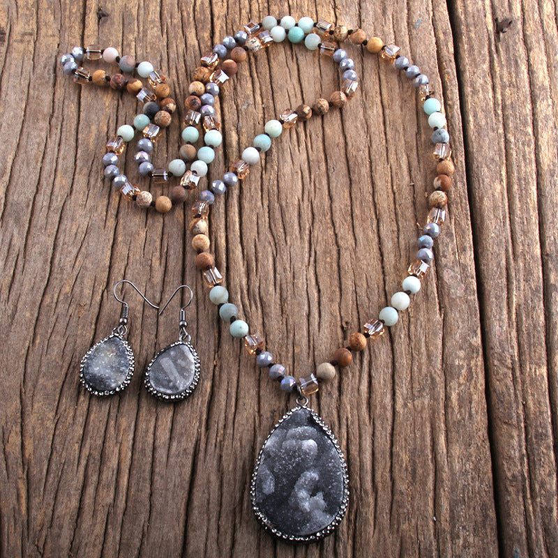 Beaded necklace and earrings with gray teardrop pendants on a wooden surface