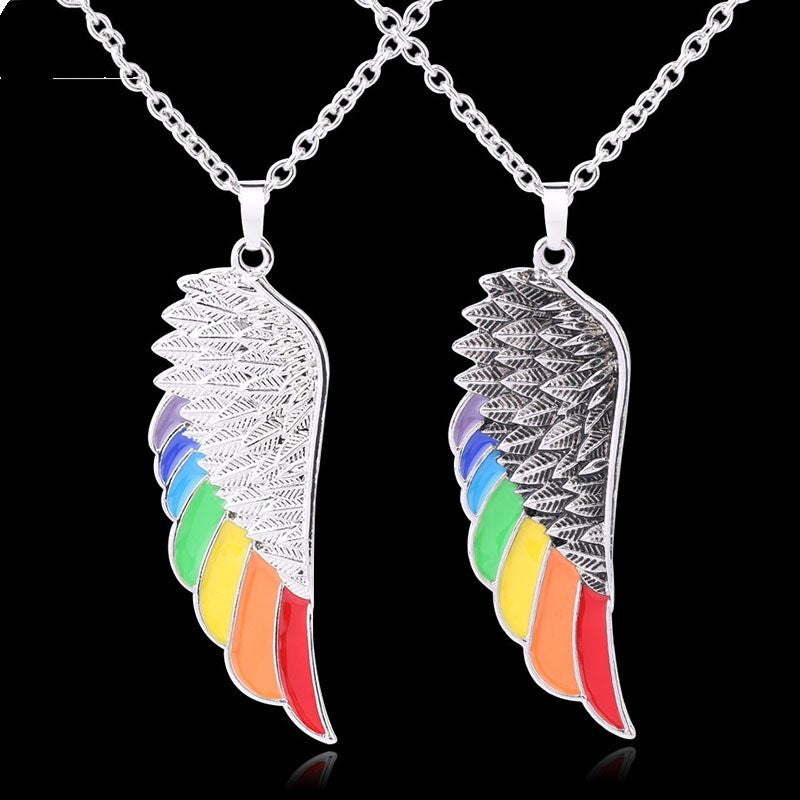 Pair of silver angel wing pendants with rainbow-colored tips on a black background