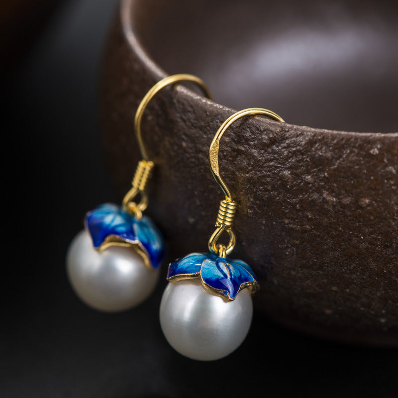 Pearl earrings with blue floral accents on a dark background