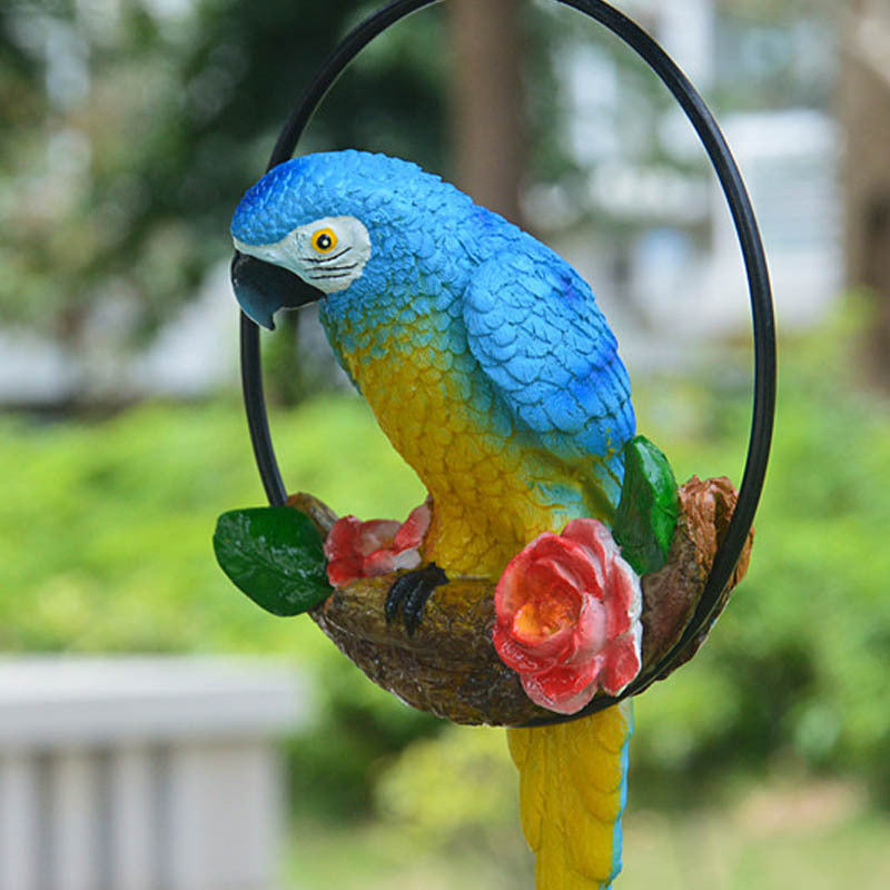 Colorful parrot figurine on a branch with flowers against a blurred green background