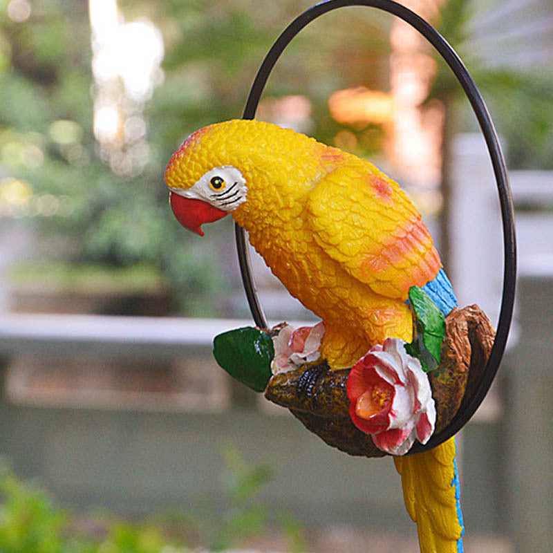 Colorful parrot figurine on a branch with flowers against a blurred green background