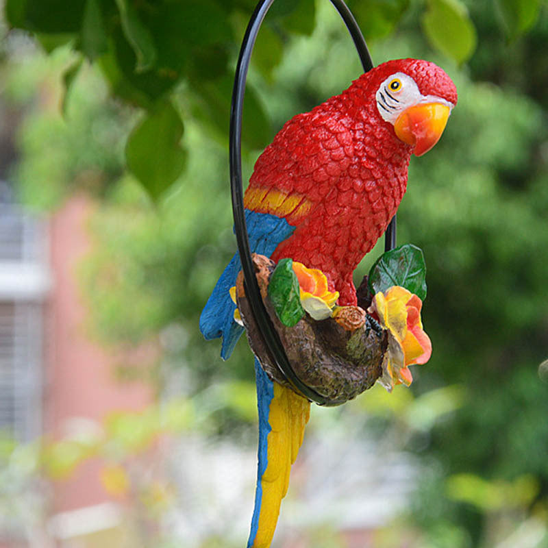 Colorful parrot figurine on a branch with leaves and flowers against a blurred green background