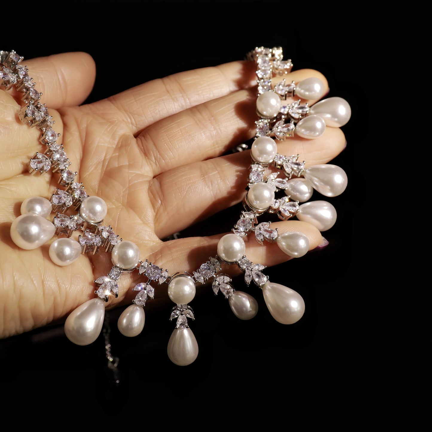Pearl necklace with teardrop-shaped pearls held by a hand against a black background