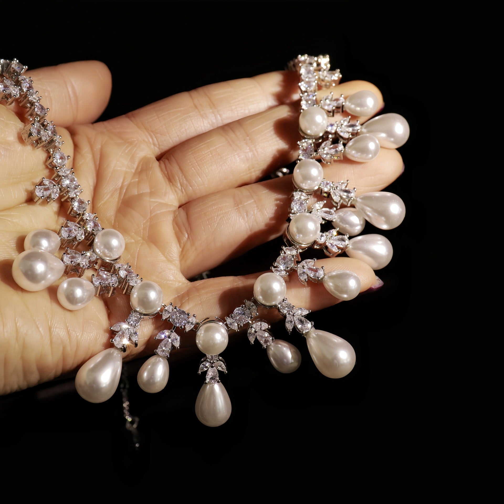 Pearl necklace with teardrop-shaped pearls held by a hand against a black background