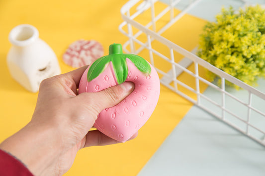 Hand holding a pink strawberry-shaped object with green leaves against a yellow and white background.