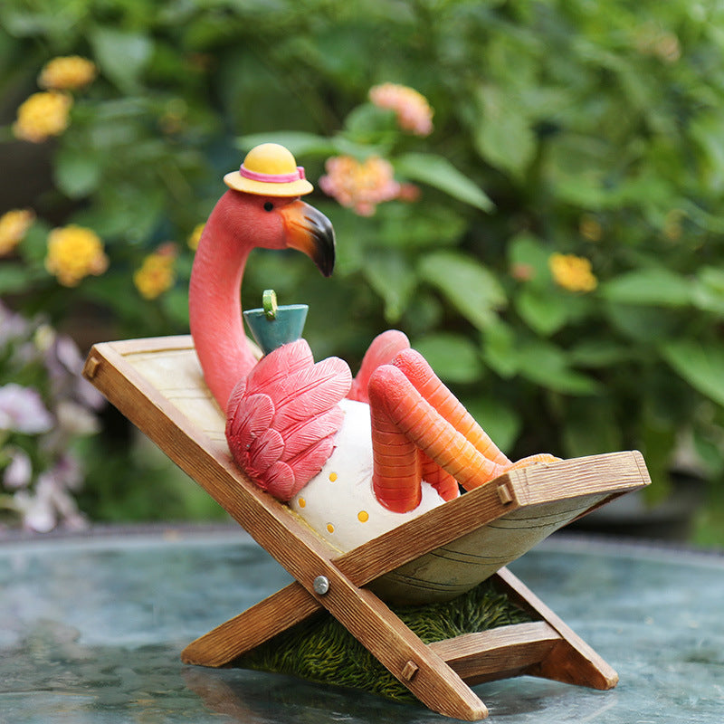 Flamingo figurine relaxing on a deck chair with a drink, outdoor setting
