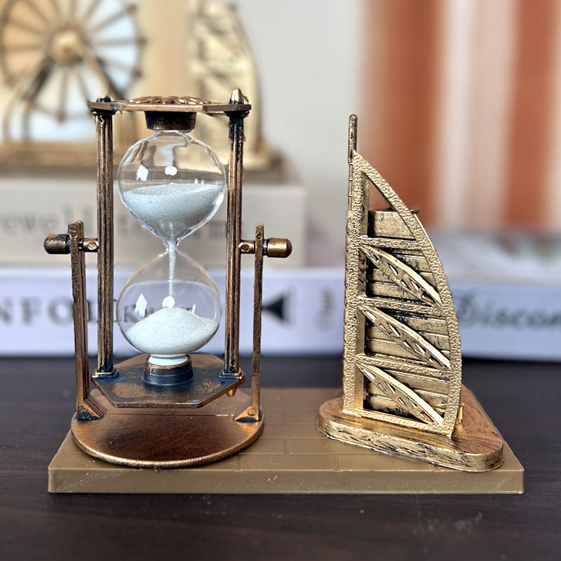 Decorative hourglass and sailboat sculpture on a dark surface with a blurred background