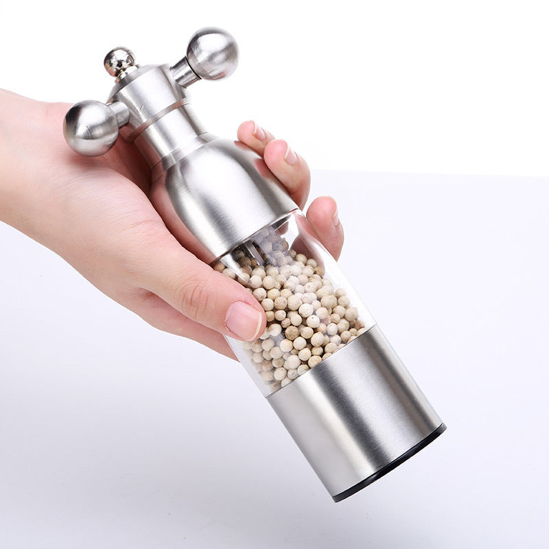 Silver pepper grinder with clear top held by a hand on a light gray background