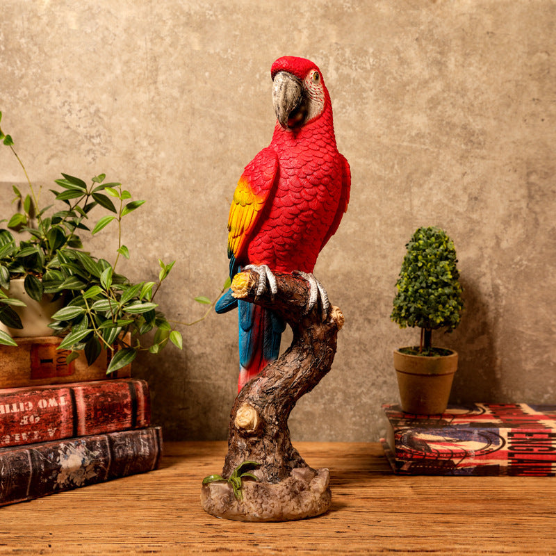 Red parrot figurine on a branch with decorative books and plants in the background