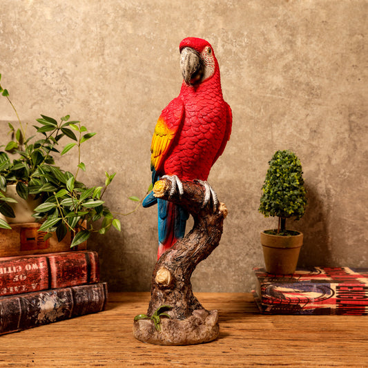 Red parrot figurine on a branch with decorative books and plants in the background
