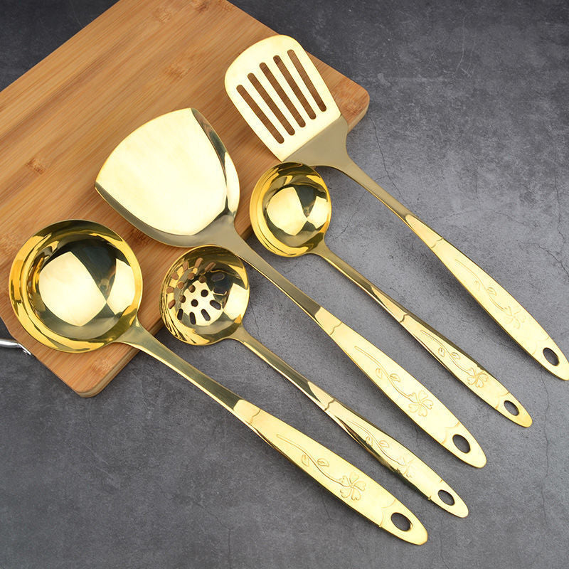 Set of gold-colored kitchen utensils on a wooden board with a gray background