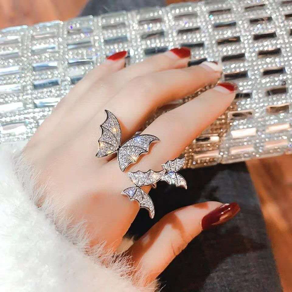 Hand wearing a butterfly-shaped ring with a sparkling clutch in the background