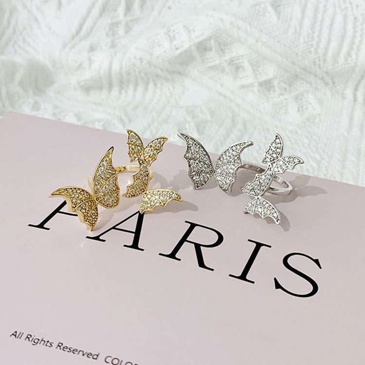 Butterfly-shaped rings in gold and silver on a white surface with 'PARIS' text.