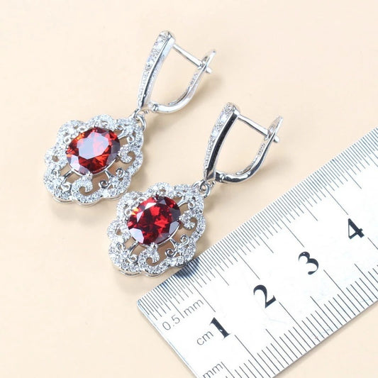 Silver earrings with red gemstones next to a ruler on a beige background