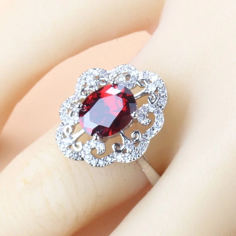 Ring with a red gemstone and silver floral design on a beige background
