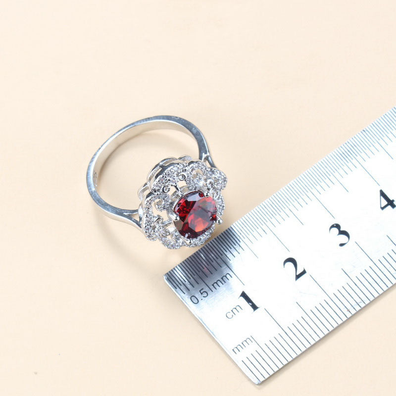 Silver ring with a red gemstone next to a ruler on a beige background