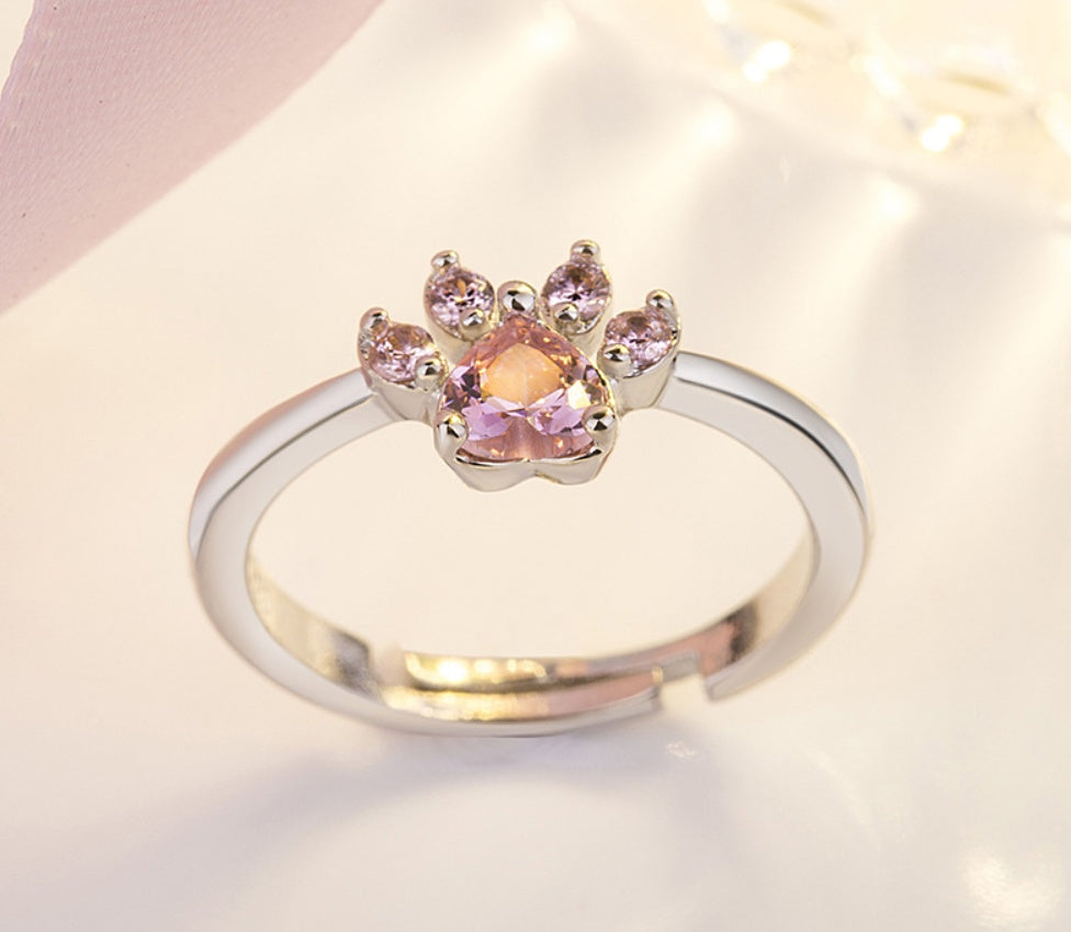 Silver ring with a paw-shaped pink gemstone on a light background