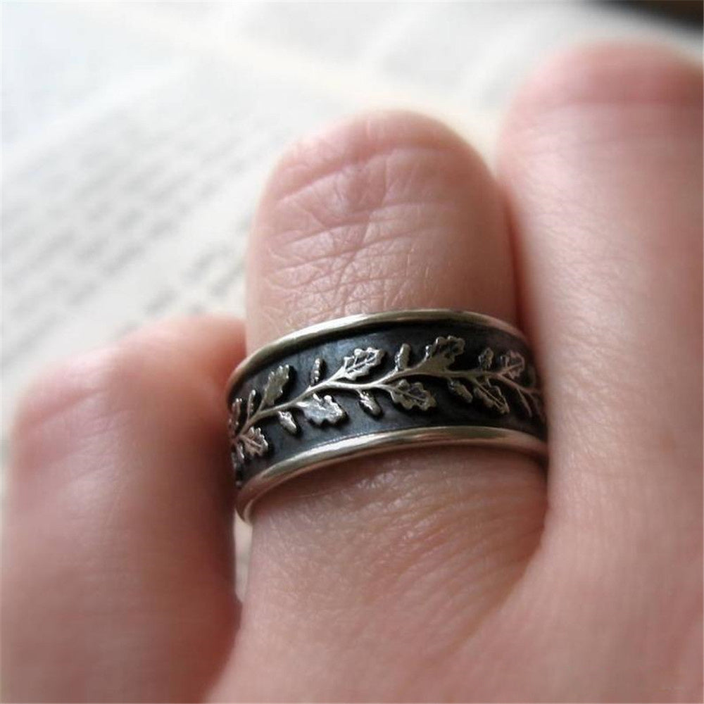 Silver ring with leaf design on a finger against a light background