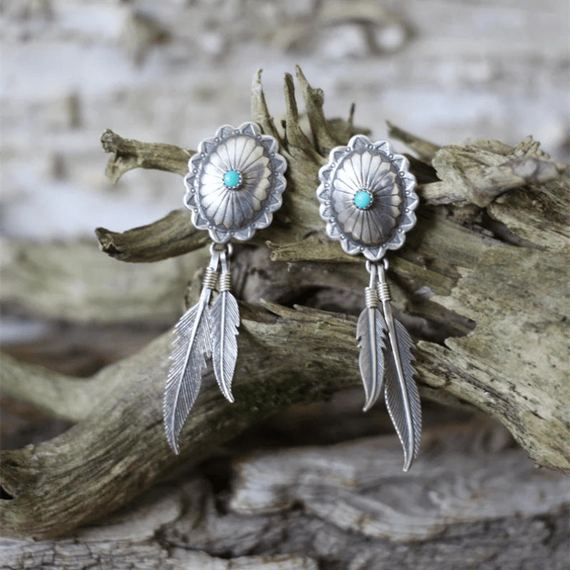 Silver concho earrings with turquoise stones and feathers on a wooden background