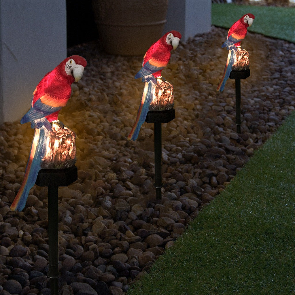 Three parrot-shaped solar lights on stakes in a garden setting.