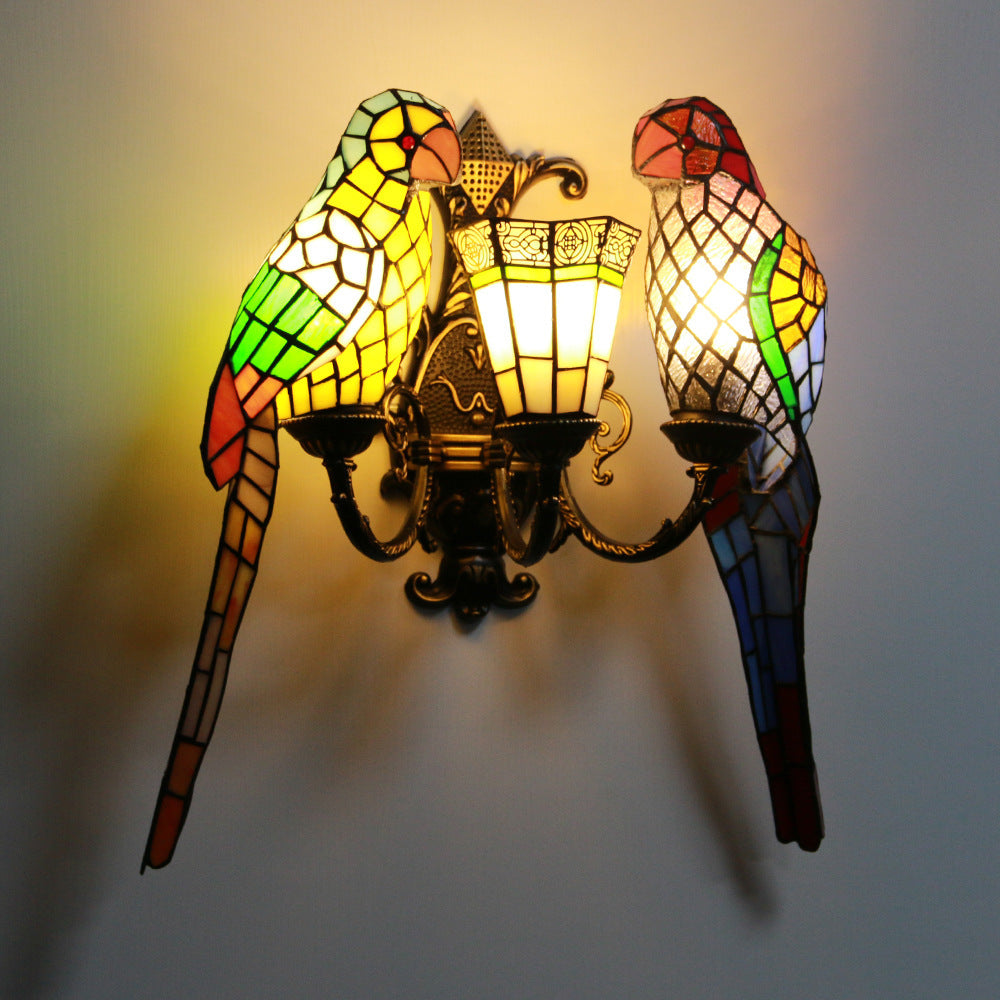 Stained glass wall sconce with parrot designs on a plain background