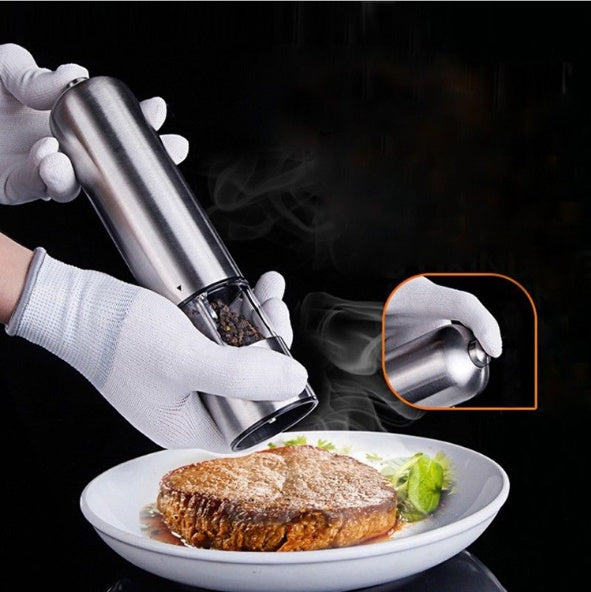 Person seasoning a dish with a pepper grinder on a black background