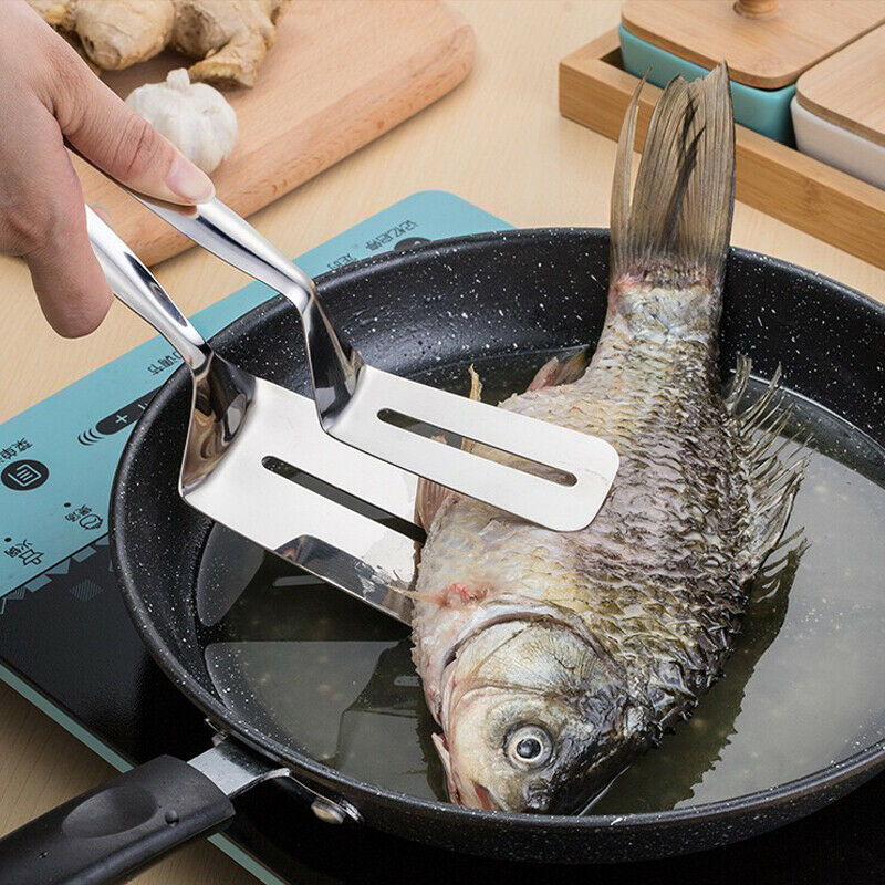 Person using a fish turner to handle a fish in a frying pan on a stove.