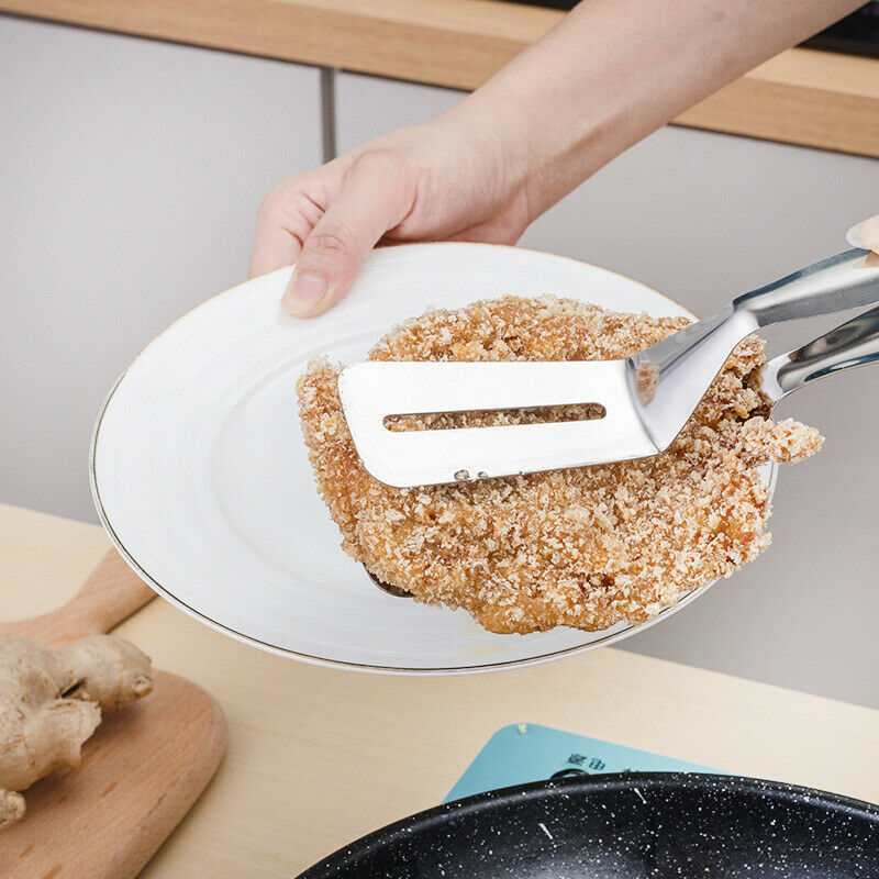 Person holding a plate with a piece of fried chicken and a spatula on a kitchen counter.