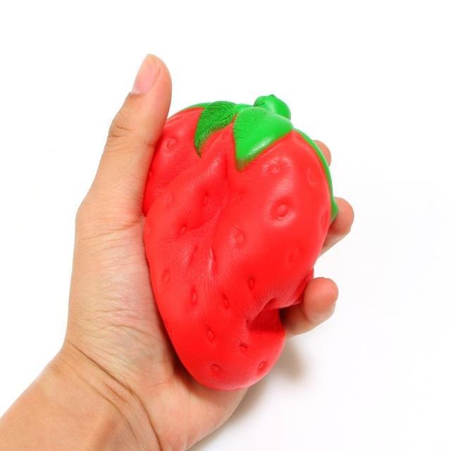 Hand holding a red strawberry-shaped squishy toy against a white background
