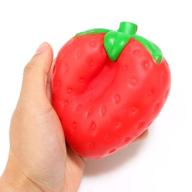 Hand holding a red pepper-shaped squishy toy with a green stem on a white background