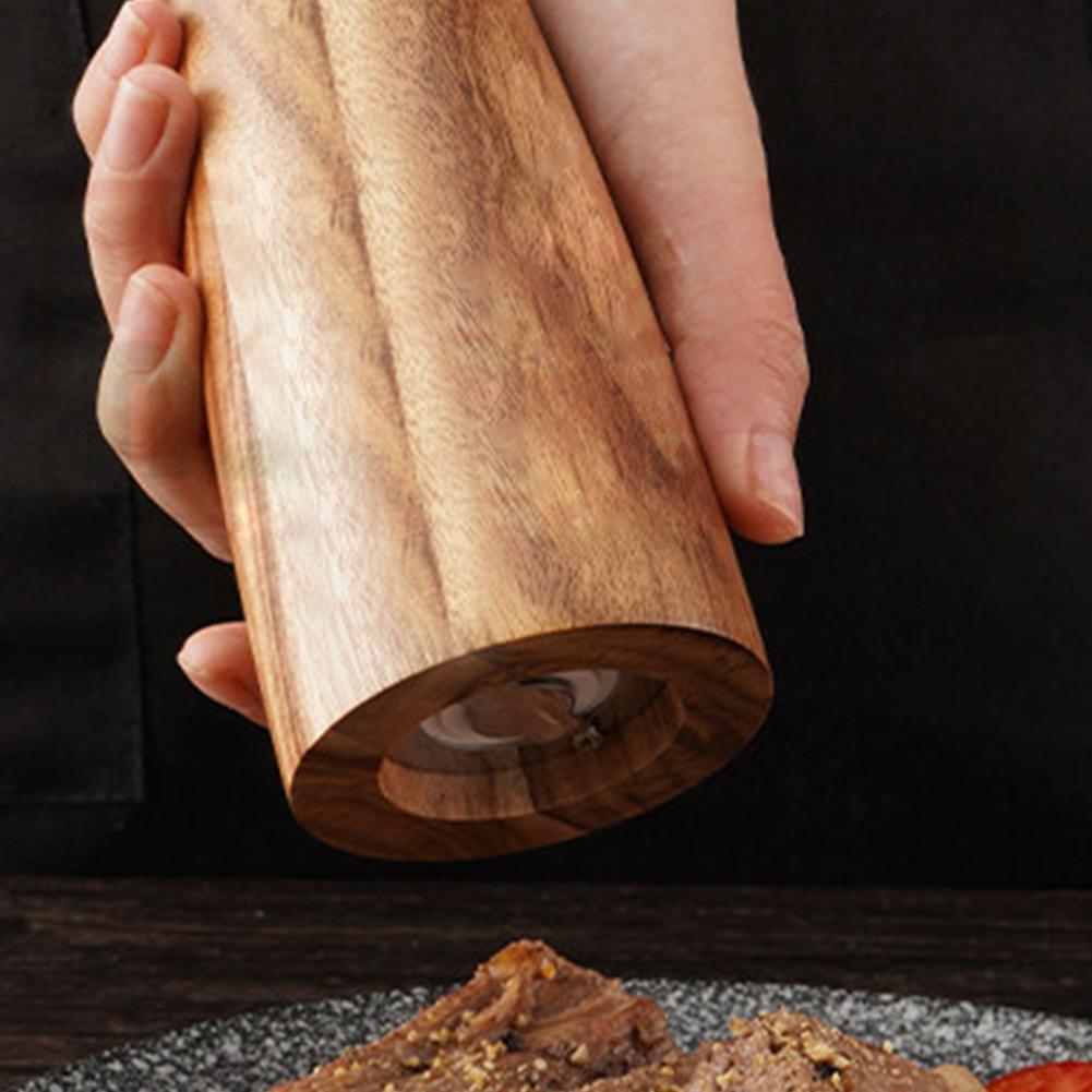 Wooden pepper grinder being held with a dark background