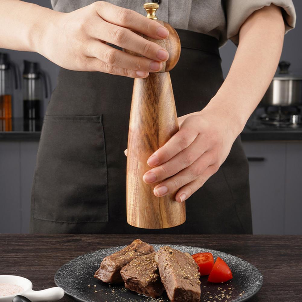 Person seasoning food with a wooden pepper grinder in a kitchen setting