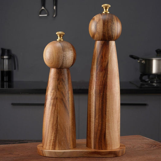 Wooden pepper grinder and salt shaker set on a kitchen counter with a dark background.