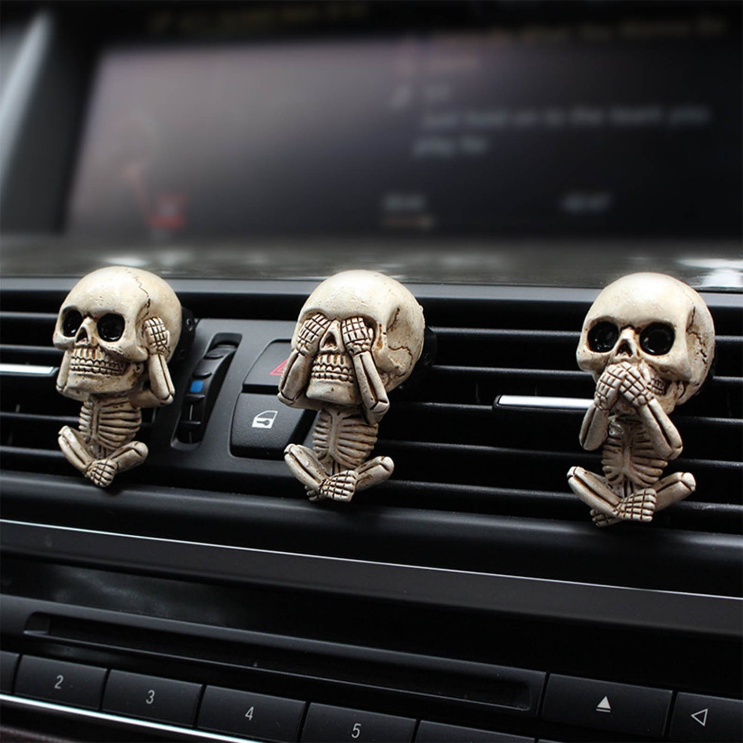 Three skeleton figurines with 'see no evil, hear no evil, speak no evil' gestures on a car dashboard.