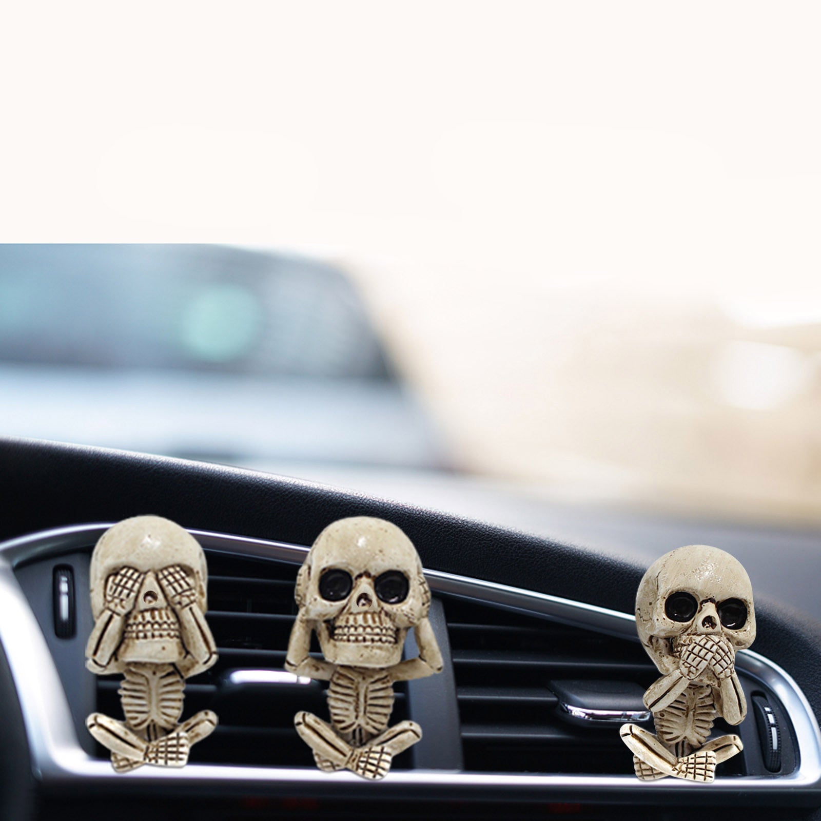 Three skull-shaped car air fresheners on a car vent with a blurred background.